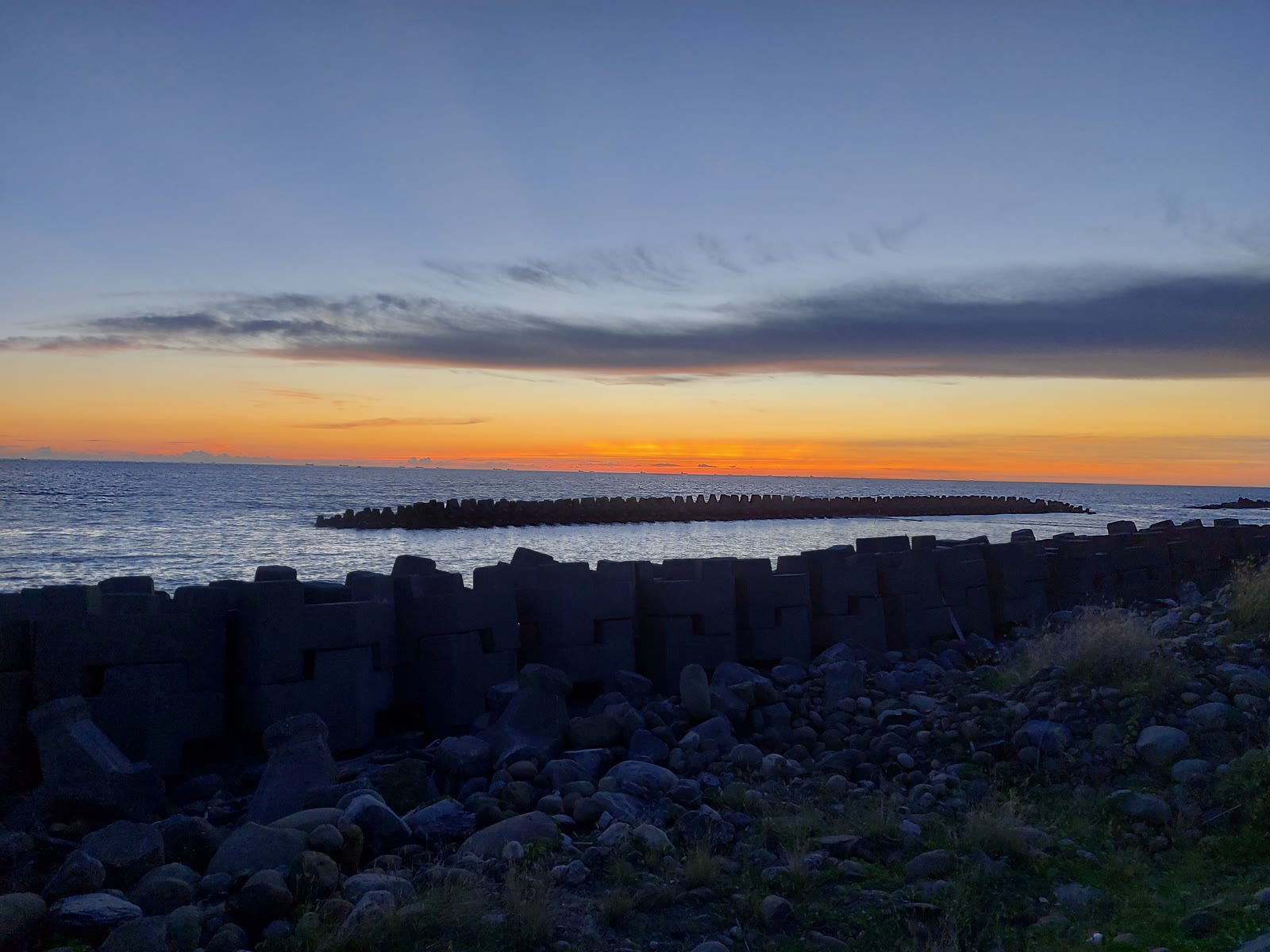 Sunset over a seawall and rocky shoreline
